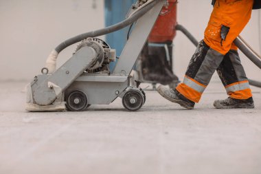 İşçiler inşaat alanındaki beton zemini öğütüyorlar. Zemini poliüretan havan topu için hazırlar