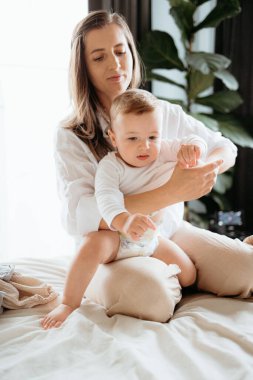 Anne, bebeğine evde bir yatakta sarılıp bakıyor.