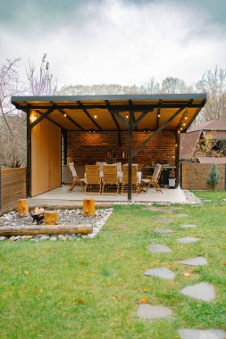 Kapalı bir avlu, ahşap yemek takımı ve sıcak bir ateş çukuru olan açık hava yaşam alanı.