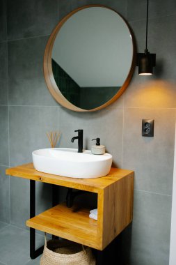 Banyo içinde şık bir lavabo, minimalist ahşap kibir ve yuvarlak ayna var.