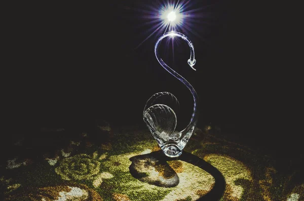 Kristal Kuğu, gece bir ışık huzmesi altında halının üzerinde duruyor..