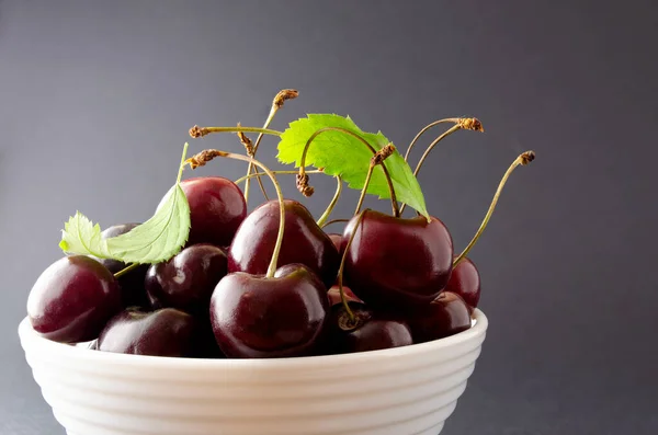 Siyah arka planda beyaz bir kasede olgun bir kiraz..