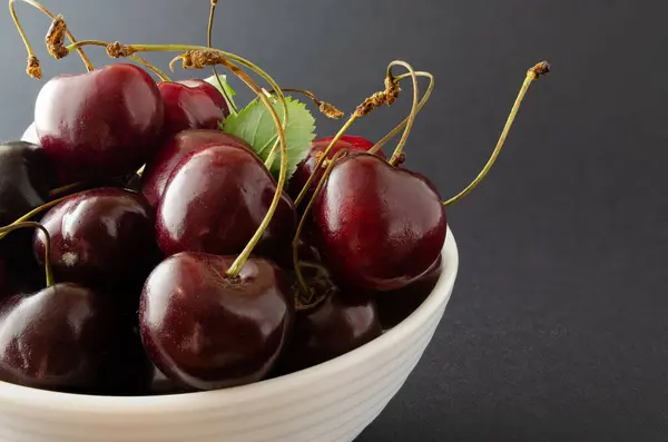 Siyah arka planda beyaz bir kasede olgun bir kiraz..