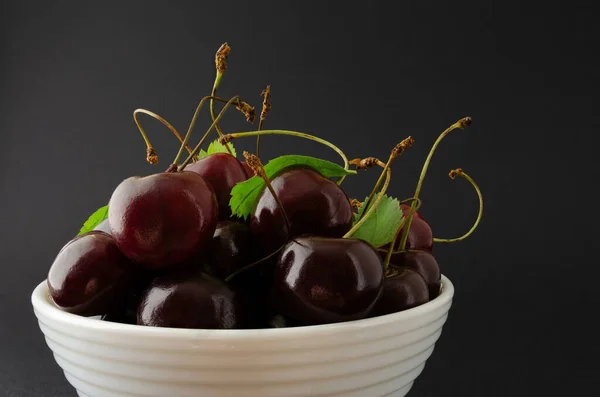 Siyah arka planda beyaz bir kasede olgun bir kiraz..