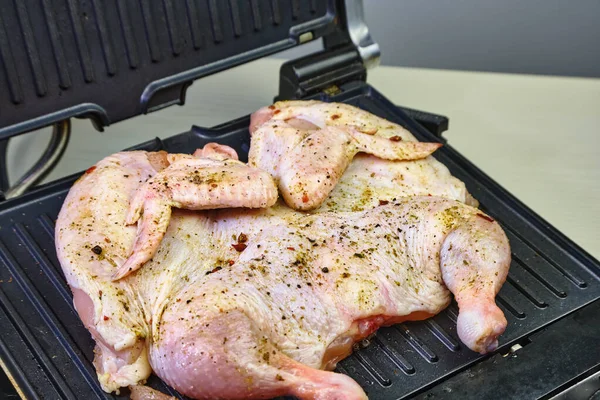 Raw chicken in seasonings lies on electric grills on home cooking. Raw grilled chicken in seasonings. Chicken meat is cooked on an electric grill on the kitchen table. close-up