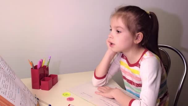 Schulmädchen, kleines brünettes Mädchen beim Unterricht im Wohnzimmer am Tisch. Auf dem Tisch liegen ein Notizbuch, ein Lehrbuch, Stifte, Schulmaterial. Russland. — Stockvideo
