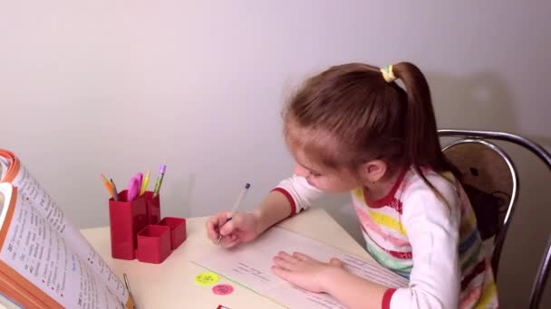 Colegiala, niña morena haciendo clases en la sala de estar en la mesa. Sobre la mesa hay un cuaderno, un libro de texto, bolígrafos, útiles escolares. Rusia. — Vídeo de stock