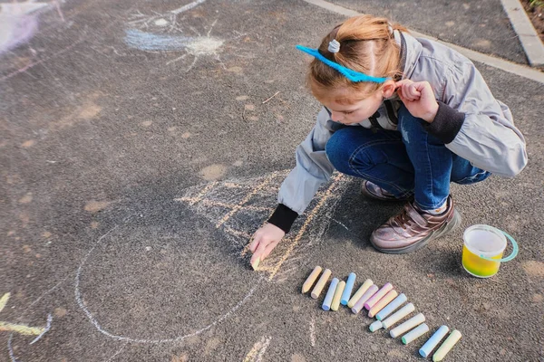 Ein glückliches Mädchen zeichnet mit bunten Buntstiften, Kreide auf dem Asphalt, auf der Straße. — Stockfoto