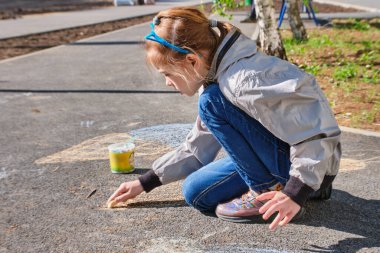 Mutlu bir kız renkli pastel boyalarla resim çizer, asfalta tebeşir çizer, sokakta..