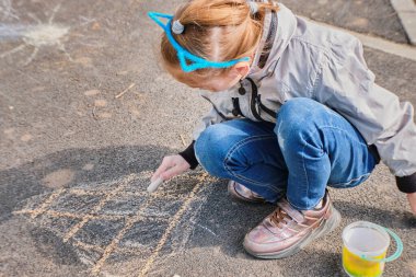 Mutlu bir kız renkli pastel boyalarla resim çizer, asfalta tebeşir çizer, sokakta..