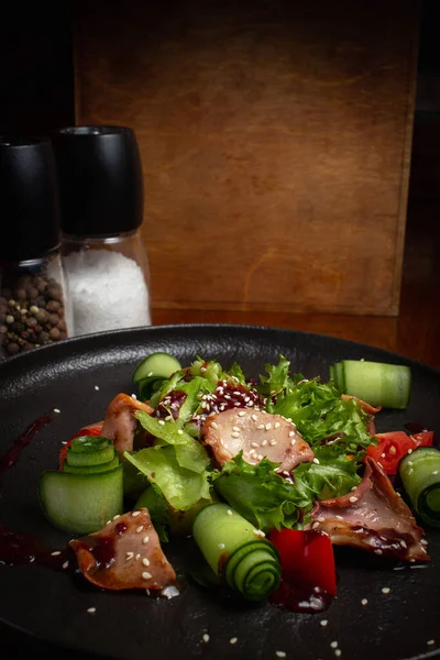 Ahtapot, domates ve salatalık siyah bir tabakta ahşap bir masada.