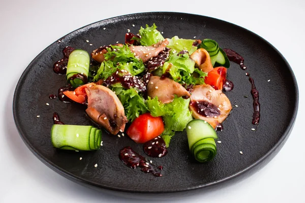 Kalamar, domates ve salatalık siyah tabakta beyaz arka planda.