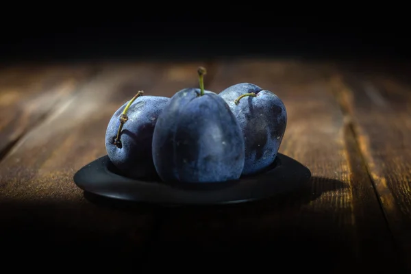 Koyu ahşap bir masada mavi erikler. Yaklaş.