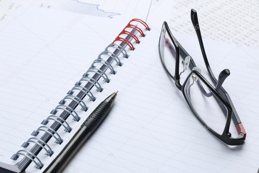 pen, notebook, glasses and financial report 