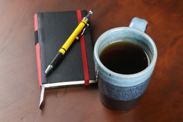 mug of tea and coffee on wood table with notebook and pen