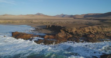 Kıyı şeridinde gün batımında kayalıkları, renkleri ve deniz fark ediliyor.