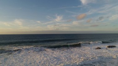 Kıyı şeridinde gün batımında kayalıkları, renkleri ve deniz fark ediliyor.