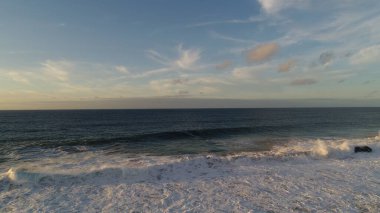 Kıyı şeridinde gün batımında kayalıkları, renkleri ve deniz fark ediliyor.