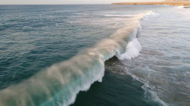 Kıyı şeridinde gün batımında kayalıkları, renkleri ve deniz fark ediliyor.