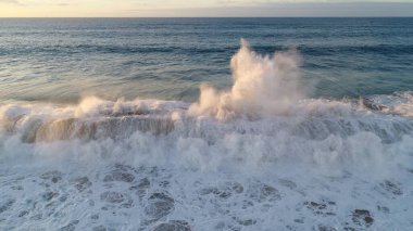 Kıyı şeridinde gün batımında kayalıkları, renkleri ve deniz fark ediliyor.