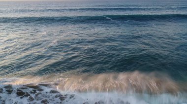 Kıyı şeridinde gün batımında kayalıkları, renkleri ve deniz fark ediliyor.