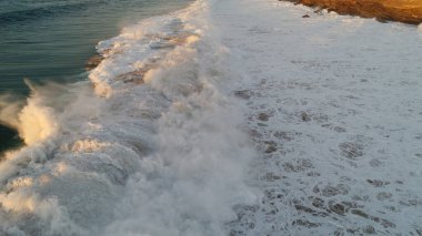 Kıyı şeridinde gün batımında kayalıkları, renkleri ve deniz fark ediliyor.