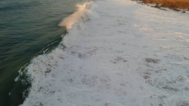 Kıyı şeridinde gün batımında kayalıkları, renkleri ve deniz fark ediliyor.