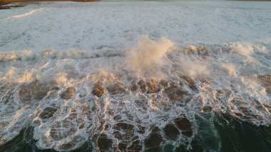 Kıyı şeridinde gün batımında kayalıkları, renkleri ve deniz fark ediliyor.