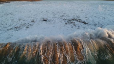 Kıyı şeridinde gün batımında kayalıkları, renkleri ve deniz fark ediliyor.