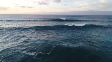 Kıyı şeridinde gün batımında kayalıkları, renkleri ve deniz fark ediliyor.