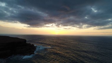 Kıyı şeridinde gün batımında kayalıkları, renkleri ve deniz fark ediliyor.