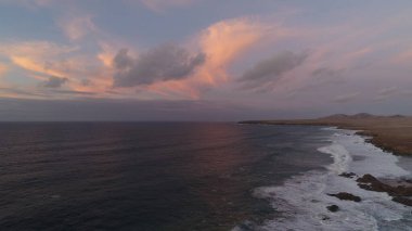 Kıyı şeridinde gün batımında kayalıkları, renkleri ve deniz fark ediliyor.