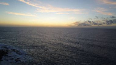 Kıyı şeridinde gün batımında kayalıkları, renkleri ve deniz fark ediliyor.