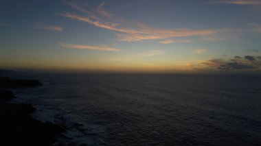 Kıyı şeridinde gün batımında kayalıkları, renkleri ve deniz fark ediliyor.