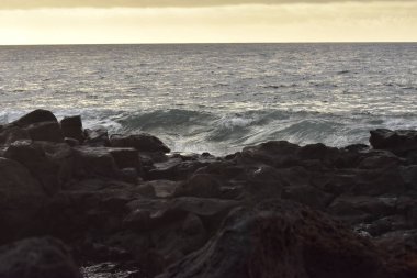 Gün batımında bir kayanın üzerinde kırılan dalgaların yakın plan çekimi.