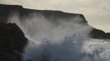 Gün batımında fırtınalı deniz, kıyıda büyük dalgalar.