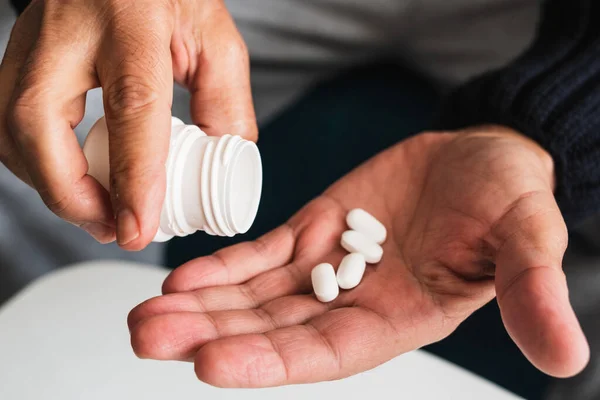 Elinde birkaç hap olan yaşlı bir adamın elleri diğer elinde taşıdığı bir konteynırdan alındı..