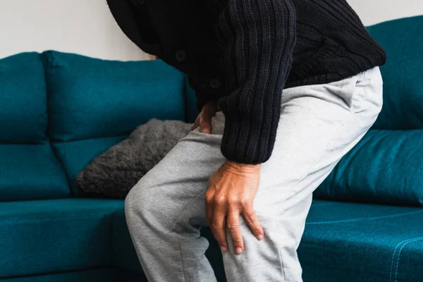 Yaşlı adam kanepeden kalktıktan sonra şiddetli ağrıdan dolayı dizine dokunur..