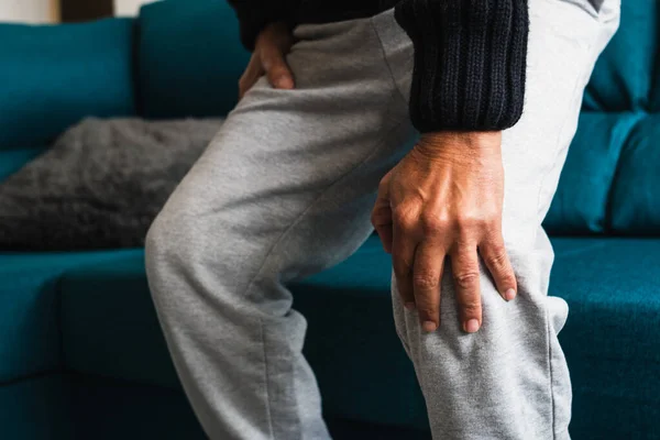 Yaşlı adam kanepeden kalktıktan sonra şiddetli ağrıdan dolayı dizine dokunur..
