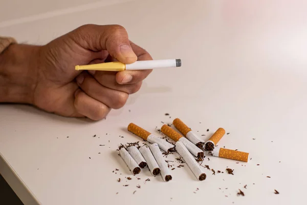 A man\'s hand holding a plastic cigarette to stop smoking, next to a pile of broken cigarettes as a sign of rejection of tobacco on a white table.
