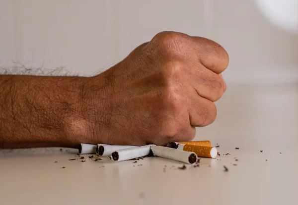 Fist of a man hitting a pile of broken cigarettes on a white table, as a sign of disapproval and rejection of tobacco. May 31, international day without tobacco.