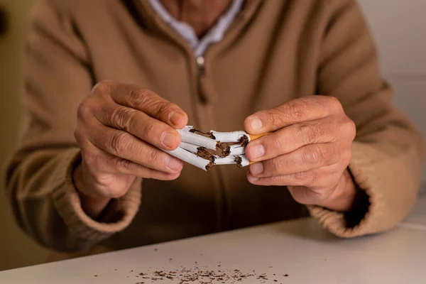 Tanımlanamayan yaşlı bir adam, dikkati dağınık, elinde bir avuç sigarayla tütünü reddederek ortadan ikiye bölünmüş..