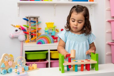 Kafkas asıllı iki yaşında bir kız, bir çekiç ve vurduğu birkaç tahta parçasıyla oynuyor, çocuk odasında..