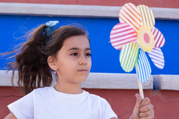 Girl with dark complexion, holding a colored pinwheel looking at it carefully