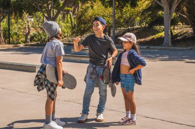 Sıradan ve şehir kıyafetleri giymiş üç beyaz kaykaycı çocuk, kaykay parkında tanıştıktan sonra birbirlerini mutlu bir şekilde selamlıyorlar..