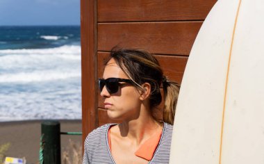 Sörf tahtasını tutan beyaz bir sörfçünün orta boy fotoğrafı.