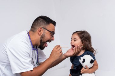 Pediyatri doktoru 3 yaşındaki bir kızın boğazını muayene ediyor.