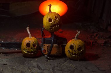 autumn holiday Halloween 2025 scary orange pumpkins with a working chainsaw in a blood red light in the dark