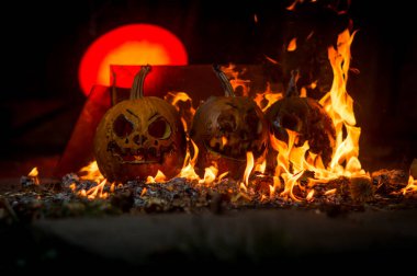 autumn holiday Halloween 2025 scary orange pumpkins burning in fire and smoke with blood red light in the dark