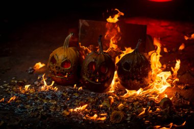autumn holiday Halloween 2025 scary orange pumpkins burning in fire and smoke with blood red light in the dark